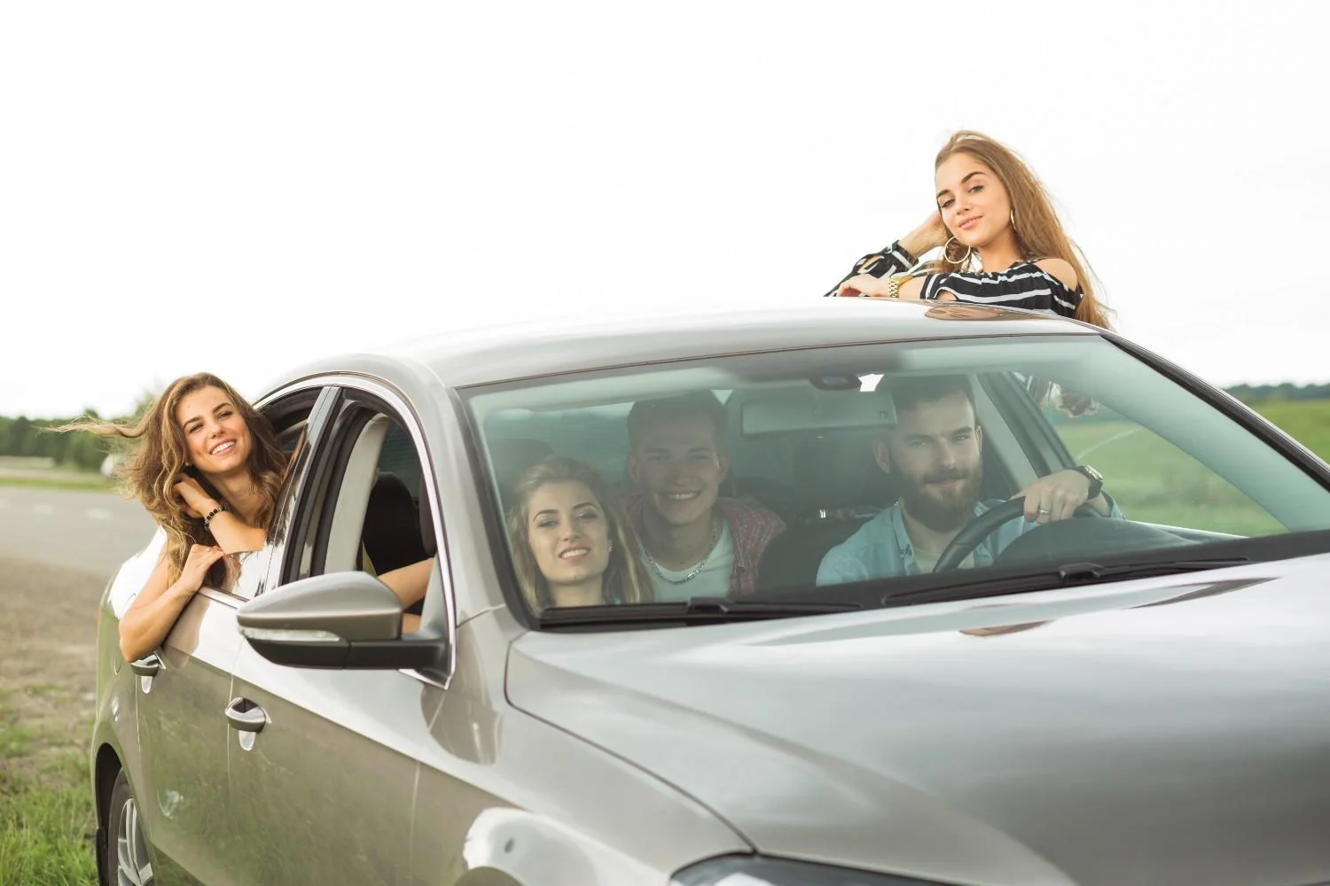 Four friends gathered around a parked car, one leaning out of the driver window
