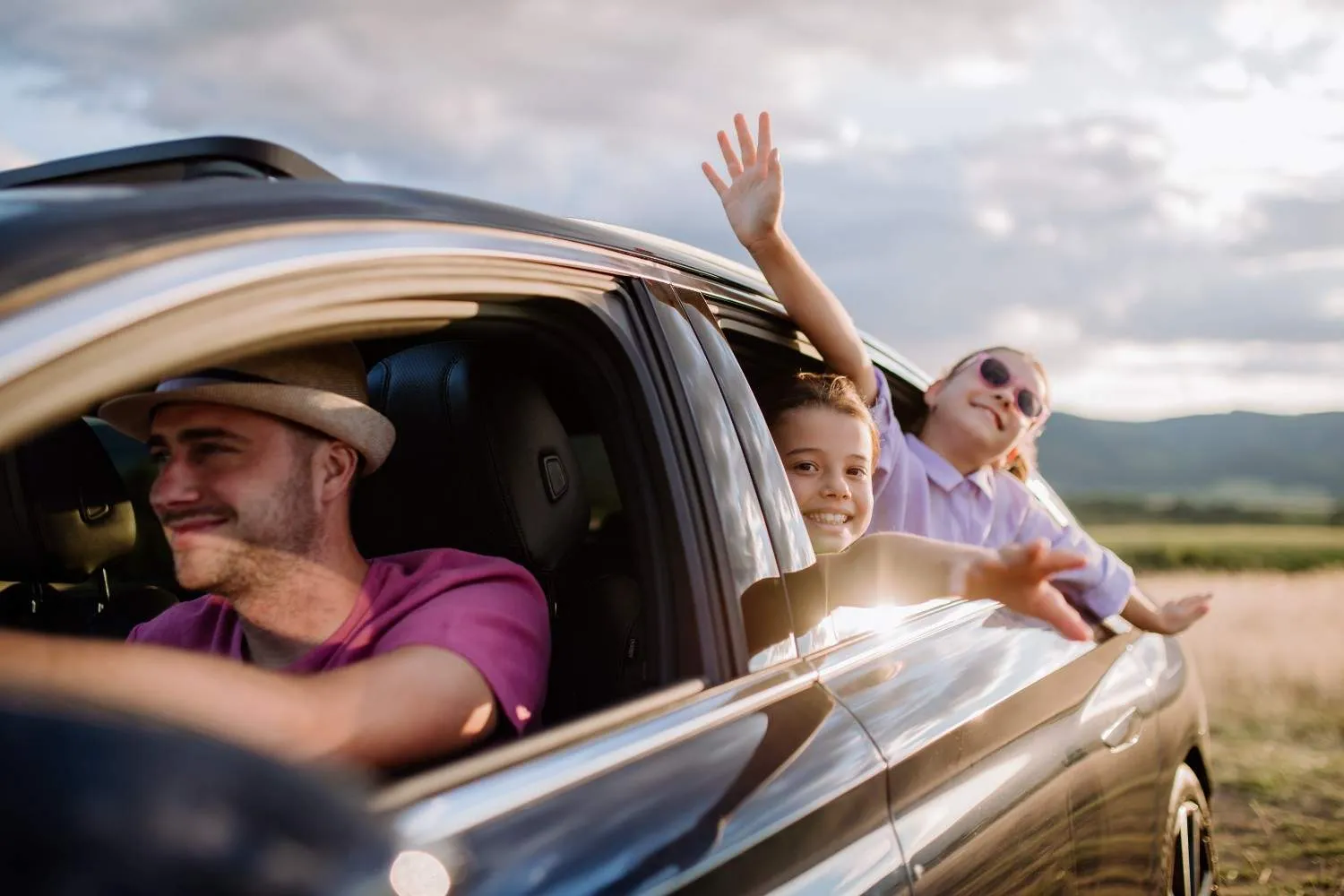 Driver at the wheel with a passenger waving out of the open car window