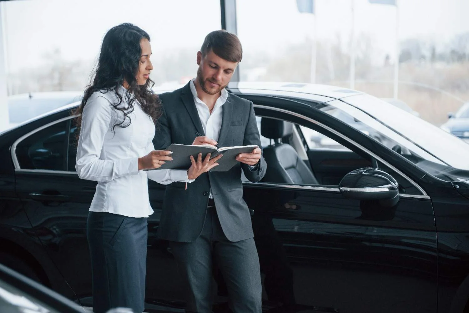 Two people standing beside a black car looking at coverage details on a tablet