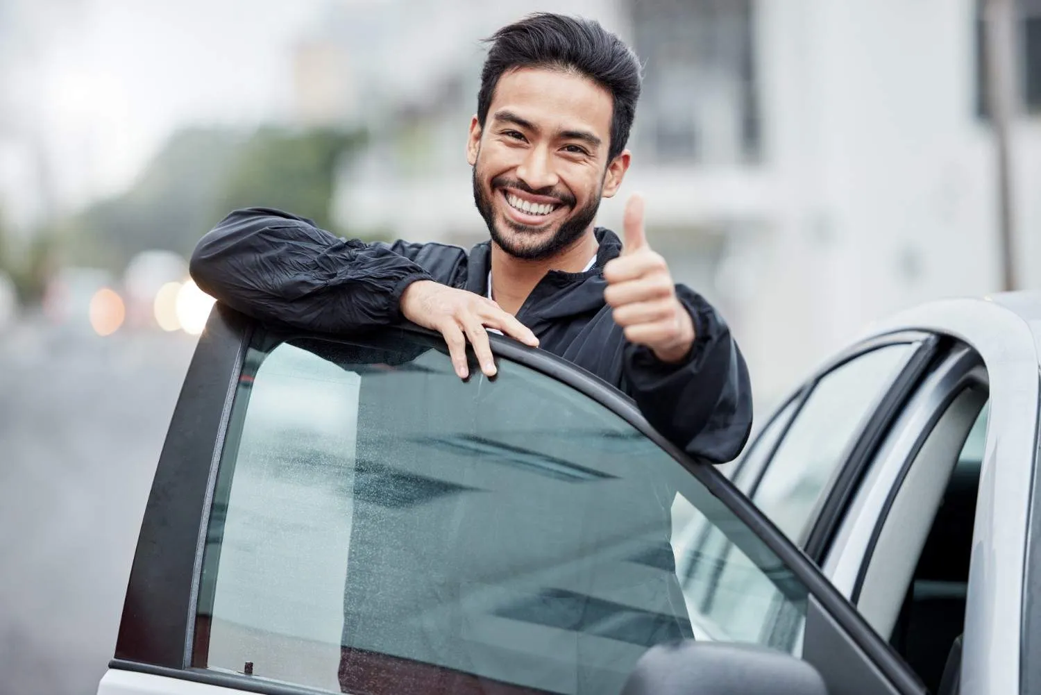 Driver leaning on an open car door giving a thumbs up
